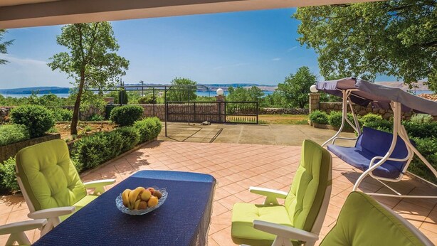 Une terrasse extérieure avec une table dressée pour le repas, des chaises et un fauteuil suspendu.