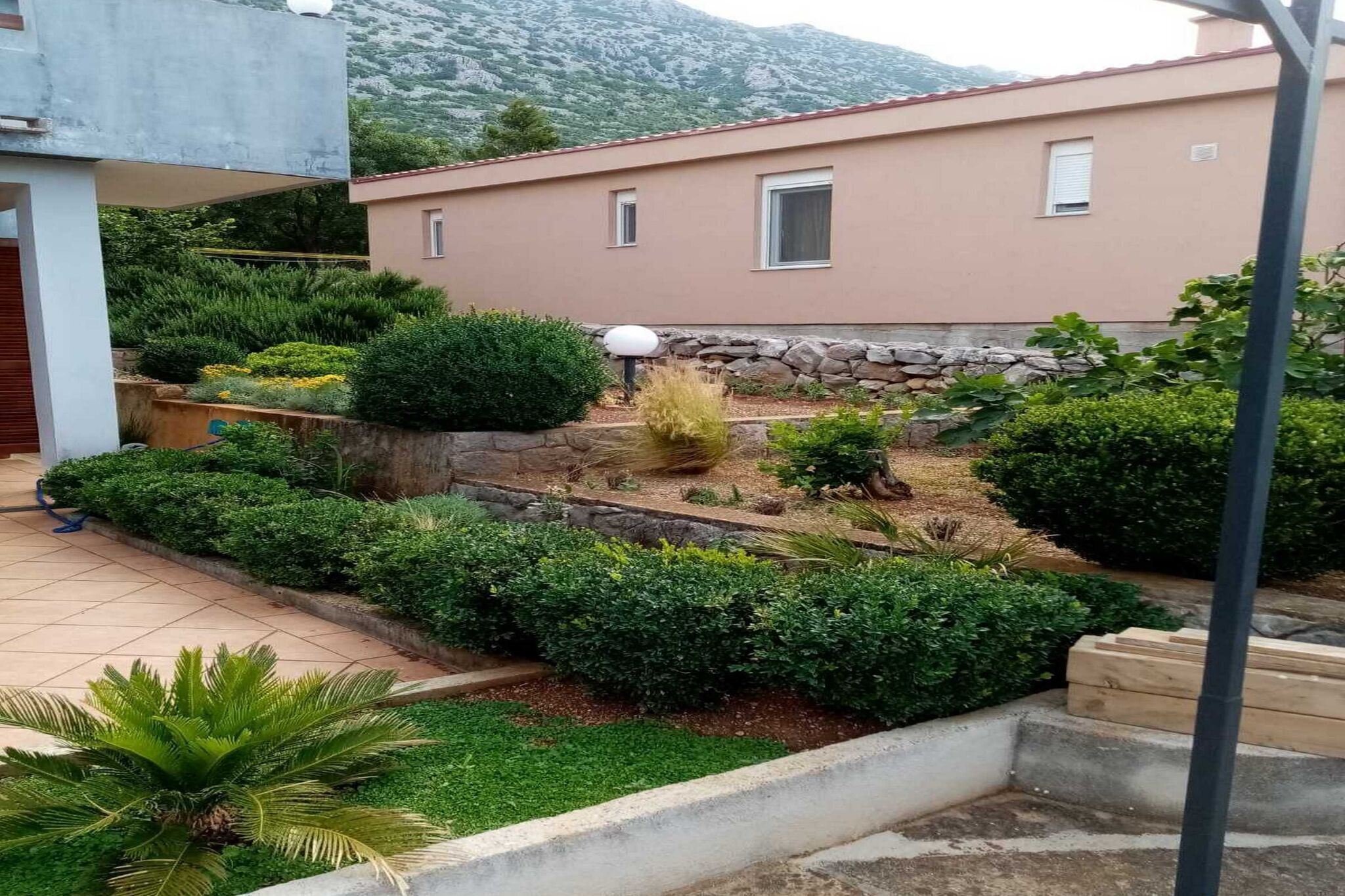 Edificio residencial con jardín, plantas variadas y muro de piedra.