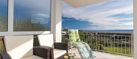 A balcony with wicker furniture, a glass table, and a view of the landscape.