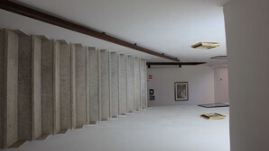 Un pasillo con una serie de pilares de concreto, techo de viga de madera y un cuadro enmarcado en la pared.