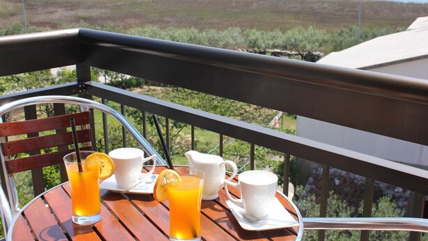 Una mesa con un vaso de jugo de naranja, una jarrón blanco y una taza blanca en un balcón con vistas a un paisaje natural.
