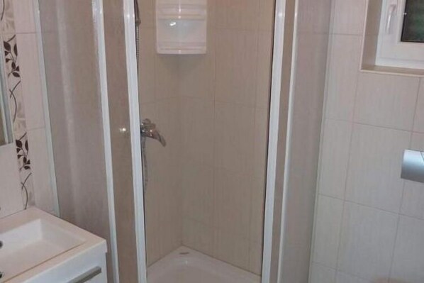 Un petit espace douche fermé, avec un mur recouvert de carreaux blancs et un seul robinet.