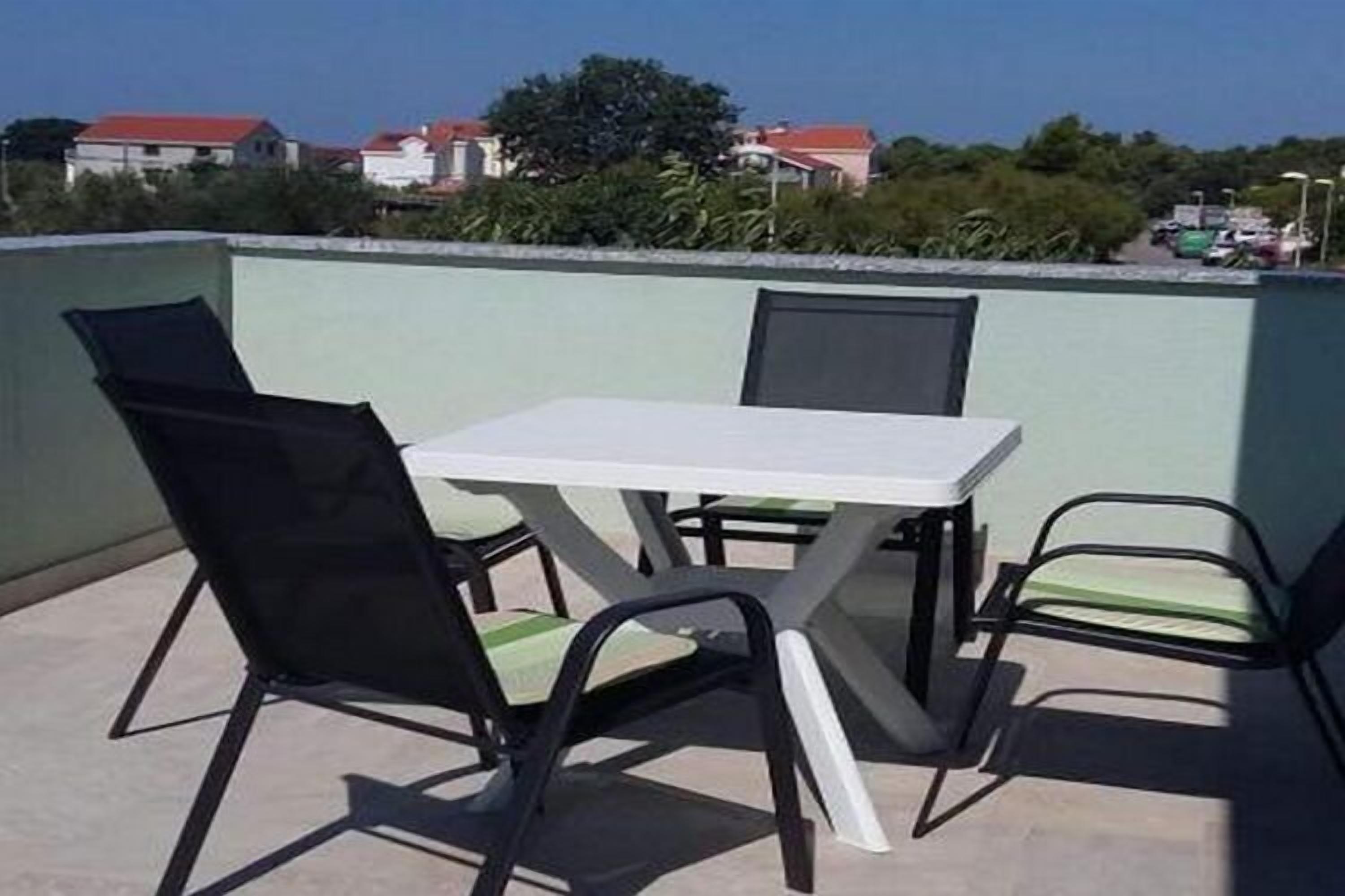 Terraço no telhado com mesa e cadeiras, rodeado por um muro baixo e vegetação ao fundo.