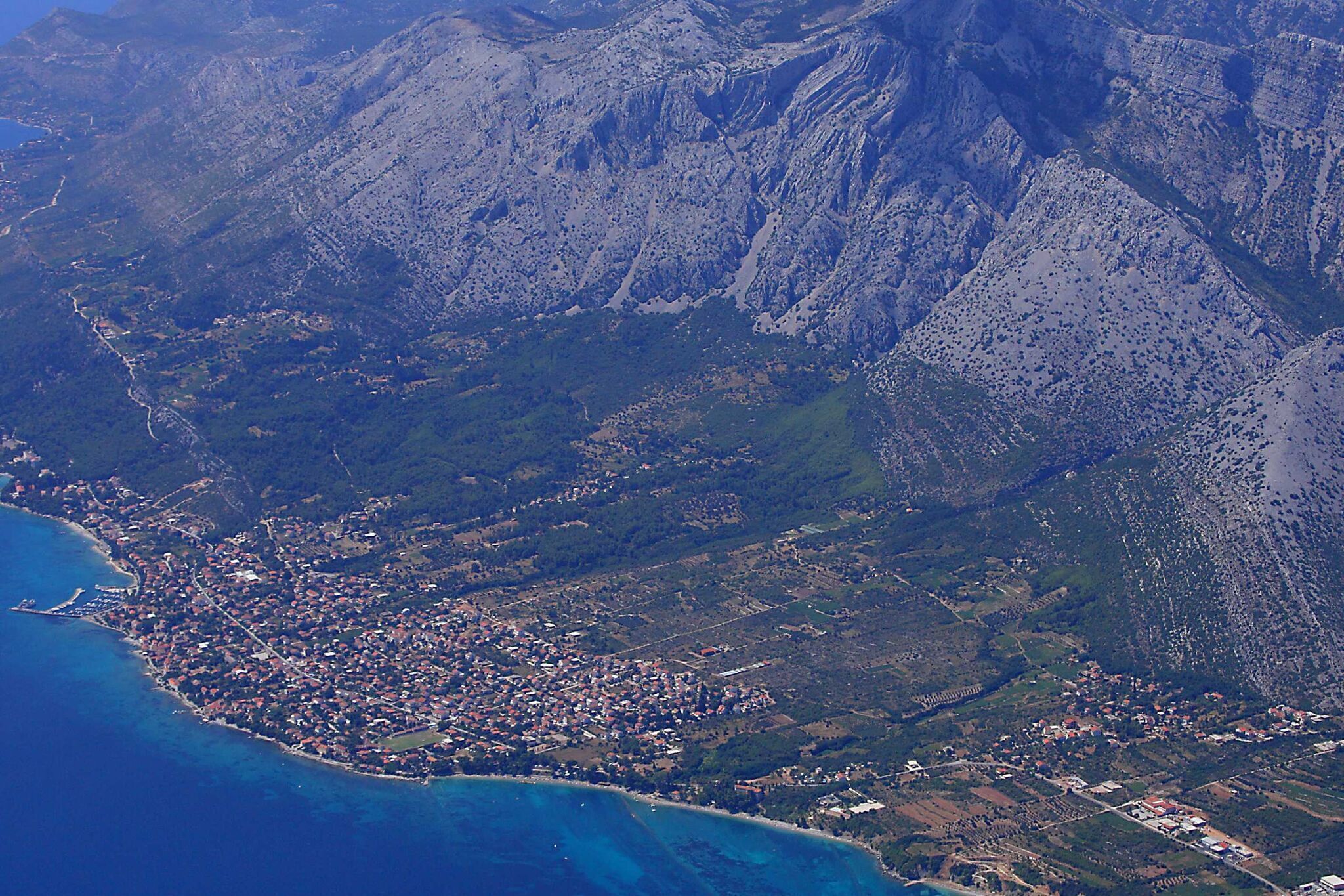 Vue aérienne d’une ville côtière, avec un paysage montagneux en arrière-plan.