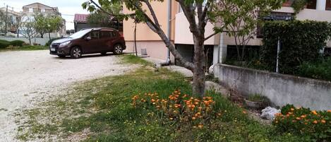 A residential area with a parked car, a tree, and a building with a balcony.
