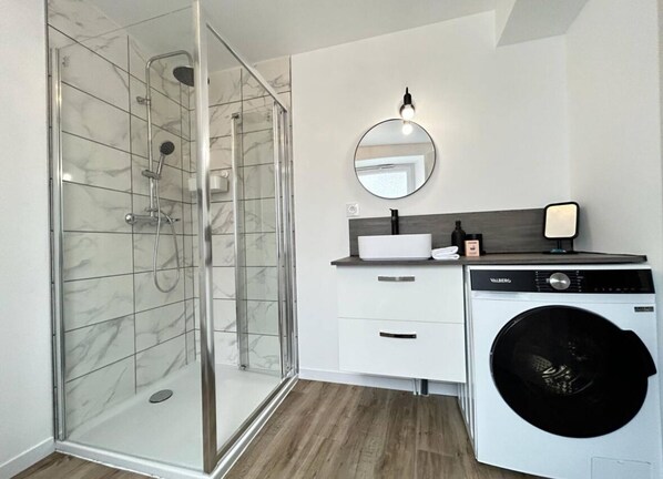 A modern bathroom with a glass-enclosed shower, a white sink with a mirror, and a front-loading washing machine. - Le Meunier, cozy new studio in Chouilly, 5 mn from Epernay. (Chouilly)