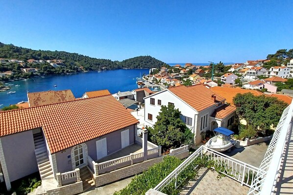 A coastal town with terracotta-roofed buildings, a marina, and a hillside with dense greenery.