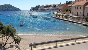Un pueblo costero con barcos amarrados a lo largo del muelle, una playa de arena y edificios con tejados de tejas rojas.