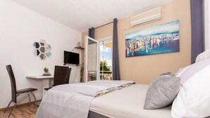 Un dormitorio con cama, escritorio, silla, televisor y un cuadro.