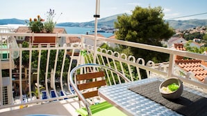 Un balcón con vistas a un pueblo costero, una piscina y un área de comedor con mesa y sillas.