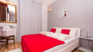 Un dormitorio con cama, mesita de noche, espejo, luz empotrada en la pared y ventana con cortinas.