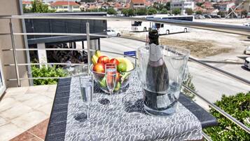 Et bord med champagneflaske, et glas og en skål med frugt på en balkon med udsigt over en vej og bygninger.