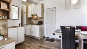 Una cocina moderna con armarios blancos, encimera de madera y horno empotrado. Hay un comedor con mesa y sillas, y una puerta que da a otra habitación.
