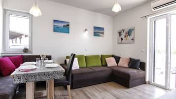 A modern living room with a dining table set for four, a brown sectional sofa with green and pink cushions, and a world map on the wall.