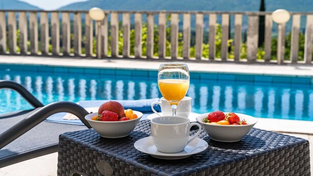 Un buffet de petit-déjeuner installé au bord d’une piscine, avec des saladiers de fruits et un verre de jus d’orange.