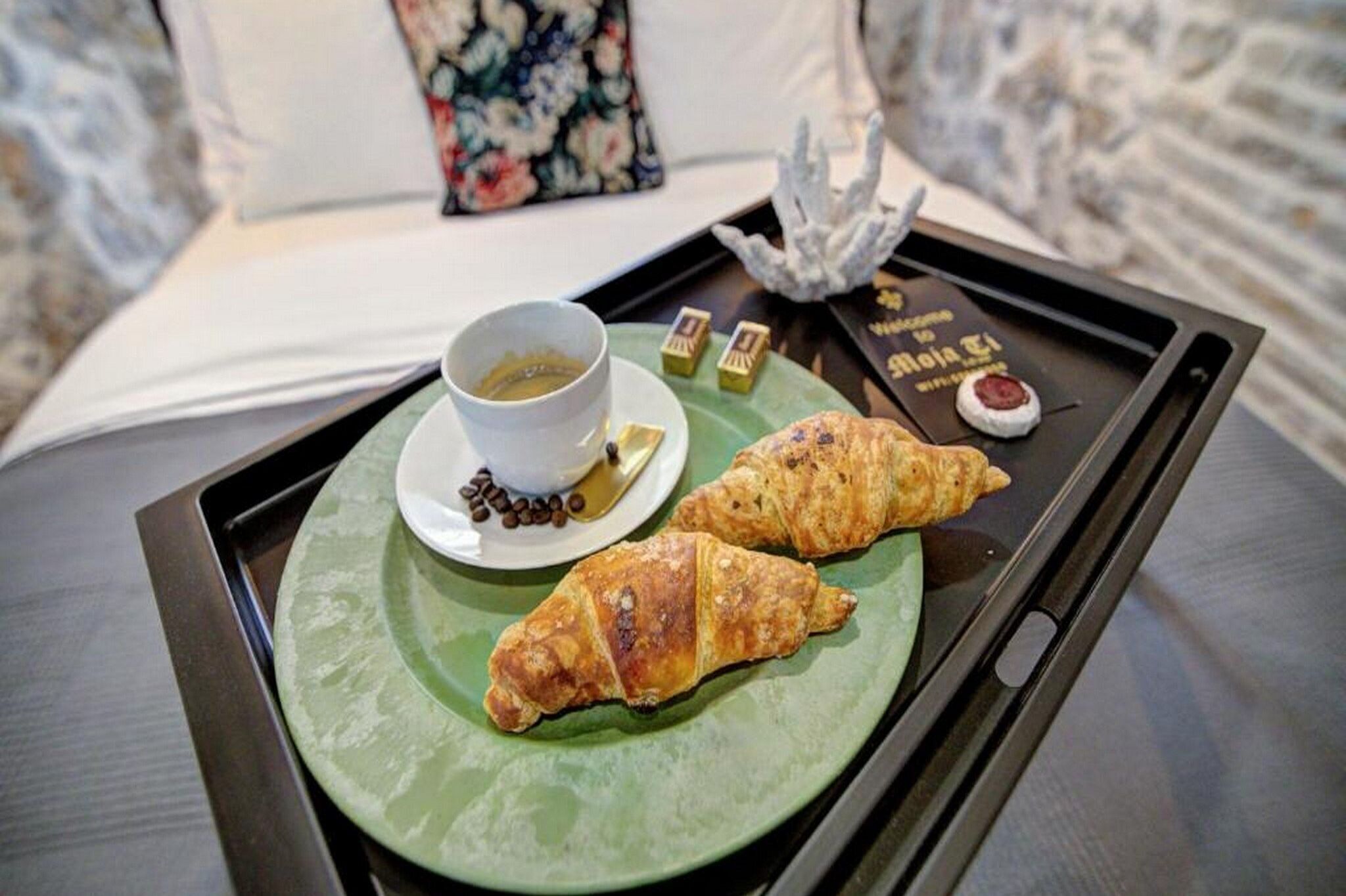 Ett bricka med croissanter, en kopp kaffe och några chokladbitar på sängen.