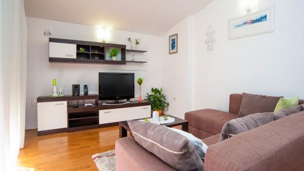 A modern living room with a flat-screen TV, a sofa set, a coffee table, and a small plant.