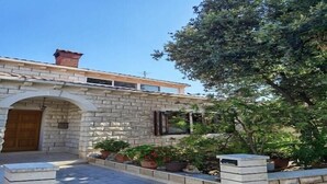Ein Steinhaus mit einer Holztür, einem Backsteinsschornstein und einem kleinen Garten mit Topfpflanzen.