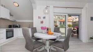A modern kitchen with white cabinets, a dining table with two chairs, and a view through a glass door to an outdoor area.