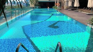 Una piscina con un diseño de mosaicos, rodeada de sillones de playa y sombrillas.
