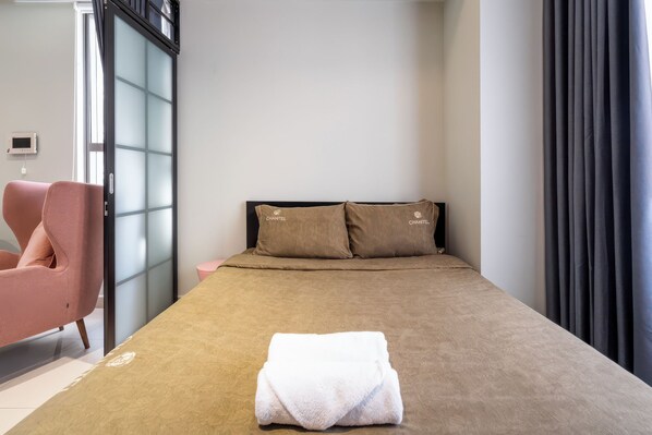 Una habitación de hotel con una cama, una silla rosa, una mesita de noche y una ventana con cortinas.