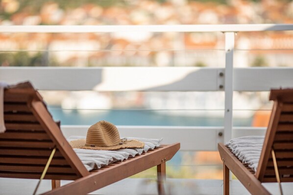 Zwei Holzliegen, auf einer ein Strohhut, mit Blick auf einen Pool.