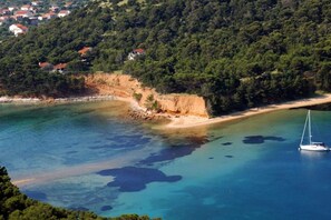 A coastal area with a sandy beach, clear blue waters, and a sailboat.