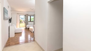 A hallway with a wooden floor leading to a room with a bed and a chair.