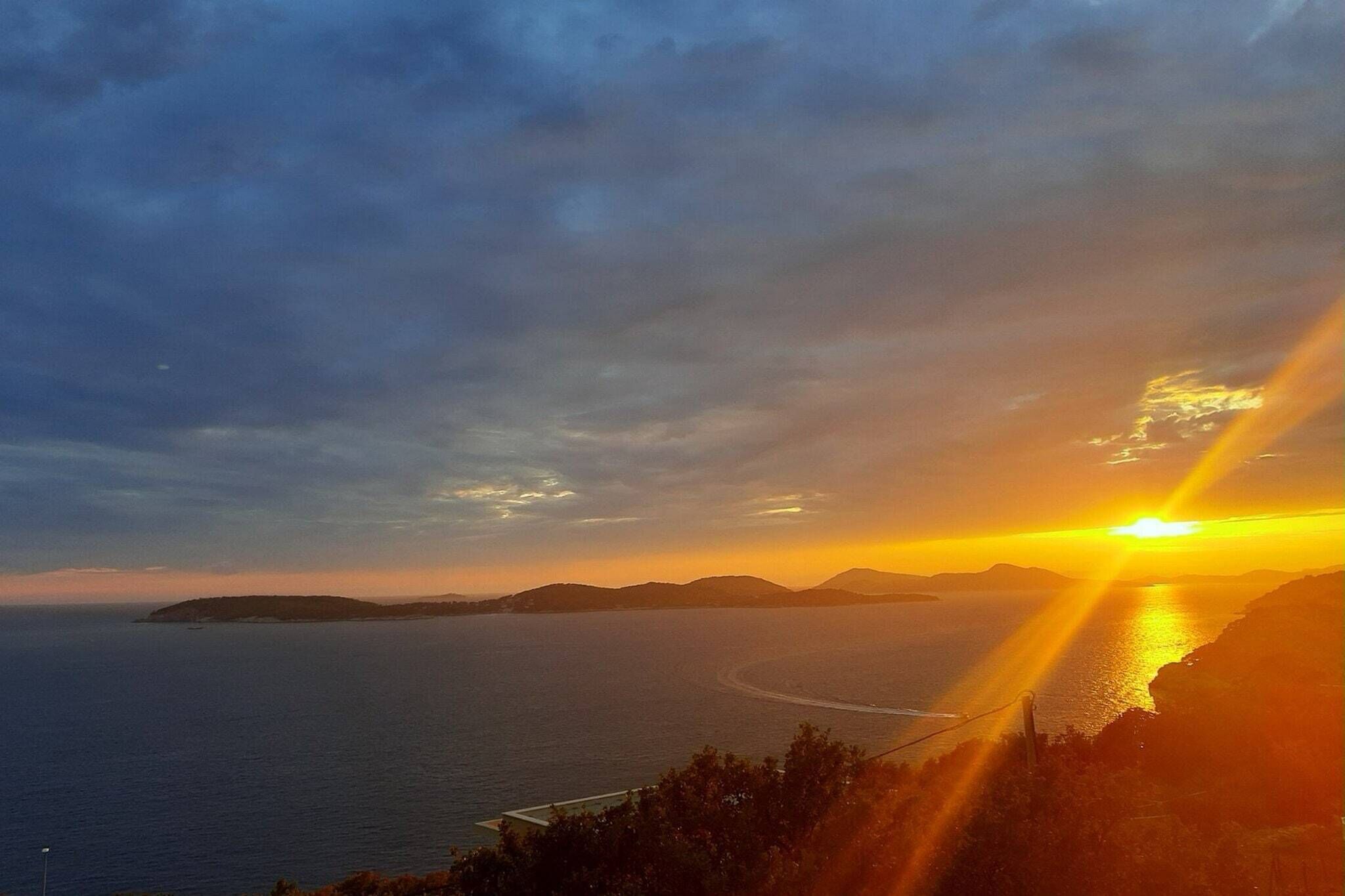 Vista de um pôr do sol na costa, com céu claro, terra ao longe e um corpo de água.