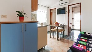A compact kitchen with blue cabinets, a dining area with a table and chairs, and a bed with a colorful bedspread. - Apartments Hak - Two Bedroom Apartment with Terrace and Sea View (Vir)