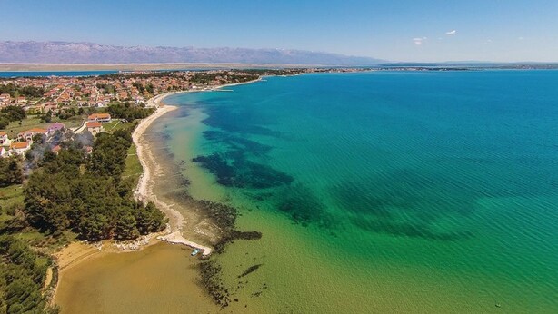 Luftaufnahme einer Küstenstadt mit blauem Meer, Sandstrand und Wohngebäuden.