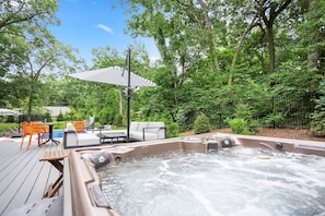 Un jacuzzi rodeado de mobiliario exterior, una piscina y un área techada con un paraguas a rayas.