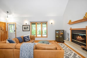 Una sala de estar con un sofá de cuero, chimenea, estantería y ventana con vista a árboles.