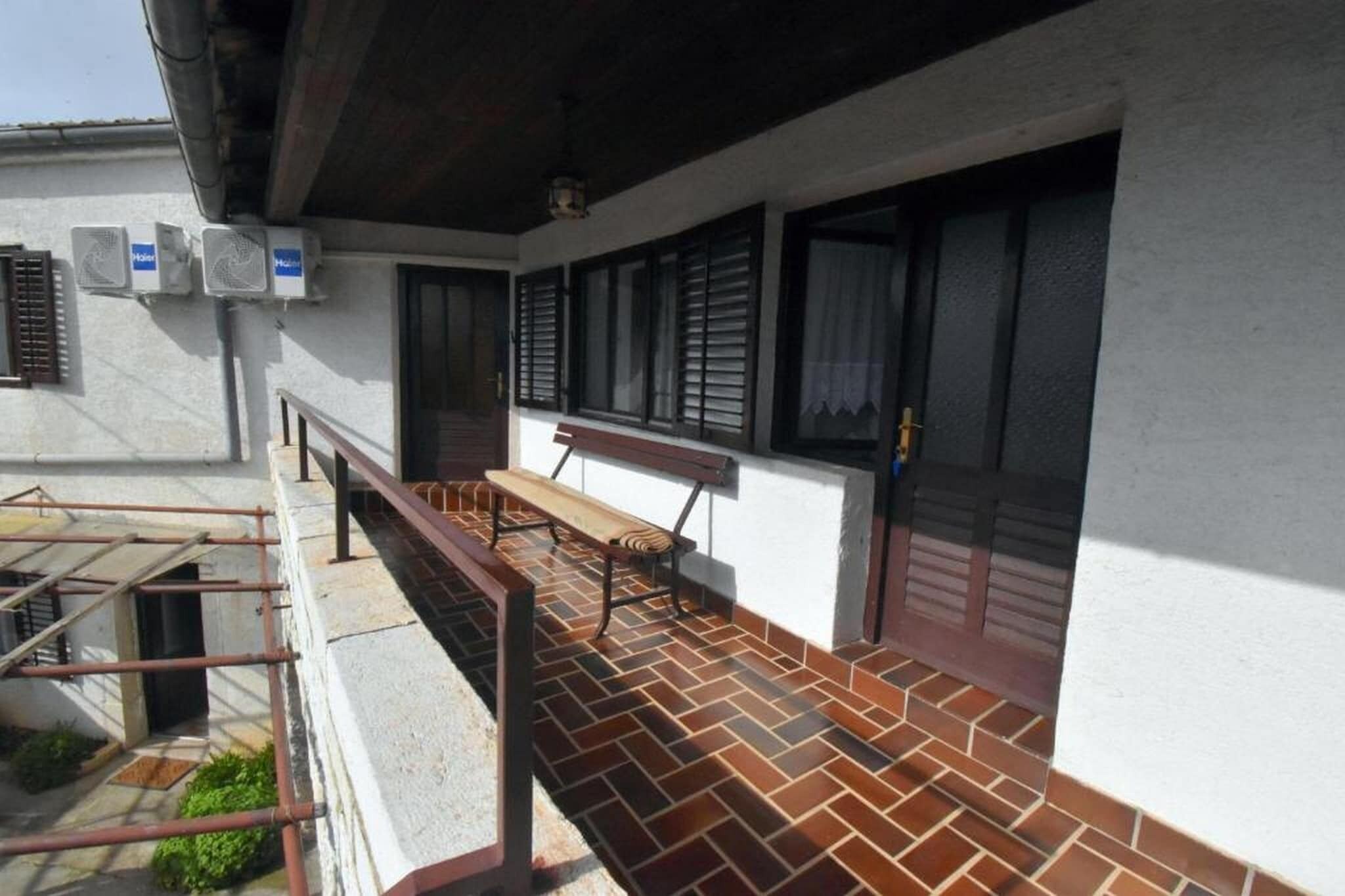 A balcony with a wooden bench, air conditioning units, and a tiled floor.