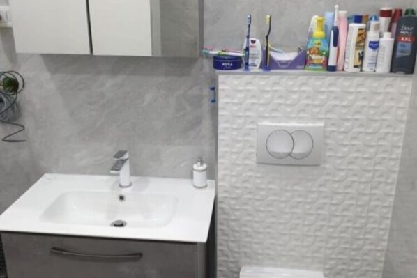 Un baño con un lavabo blanco, un perchero y un estante con artículos de aseo.