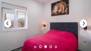 A bedroom with a bed, a window, a painting of a lion, and wall-mounted lights.