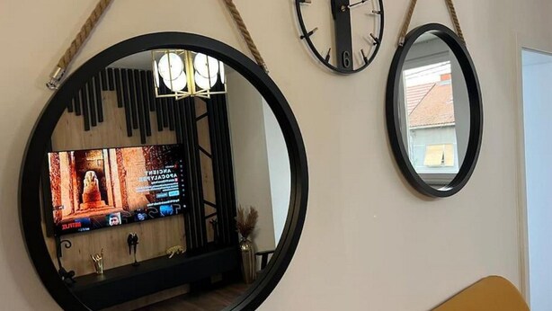 Une pièce avec un téléviseur fixé au mur, deux horloges et un miroir.