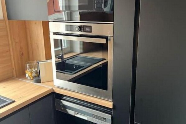 A kitchen with a built-in oven and microwave, wooden countertop, and a glass container on the counter.