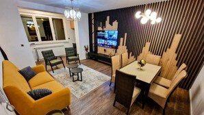 Un salon moderne comprenant un canapé, des fauteuils, une table à manger et un téléviseur fixé à un mur en bois.
