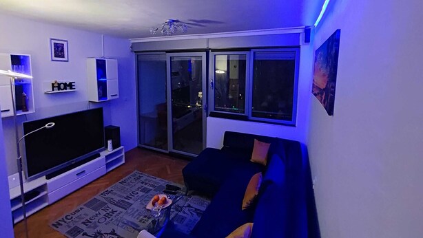 A modern living room with a flat-screen TV, a sofa, and a glass door leading to a balcony. - Apartment Sunrise (Dugi Rat)
