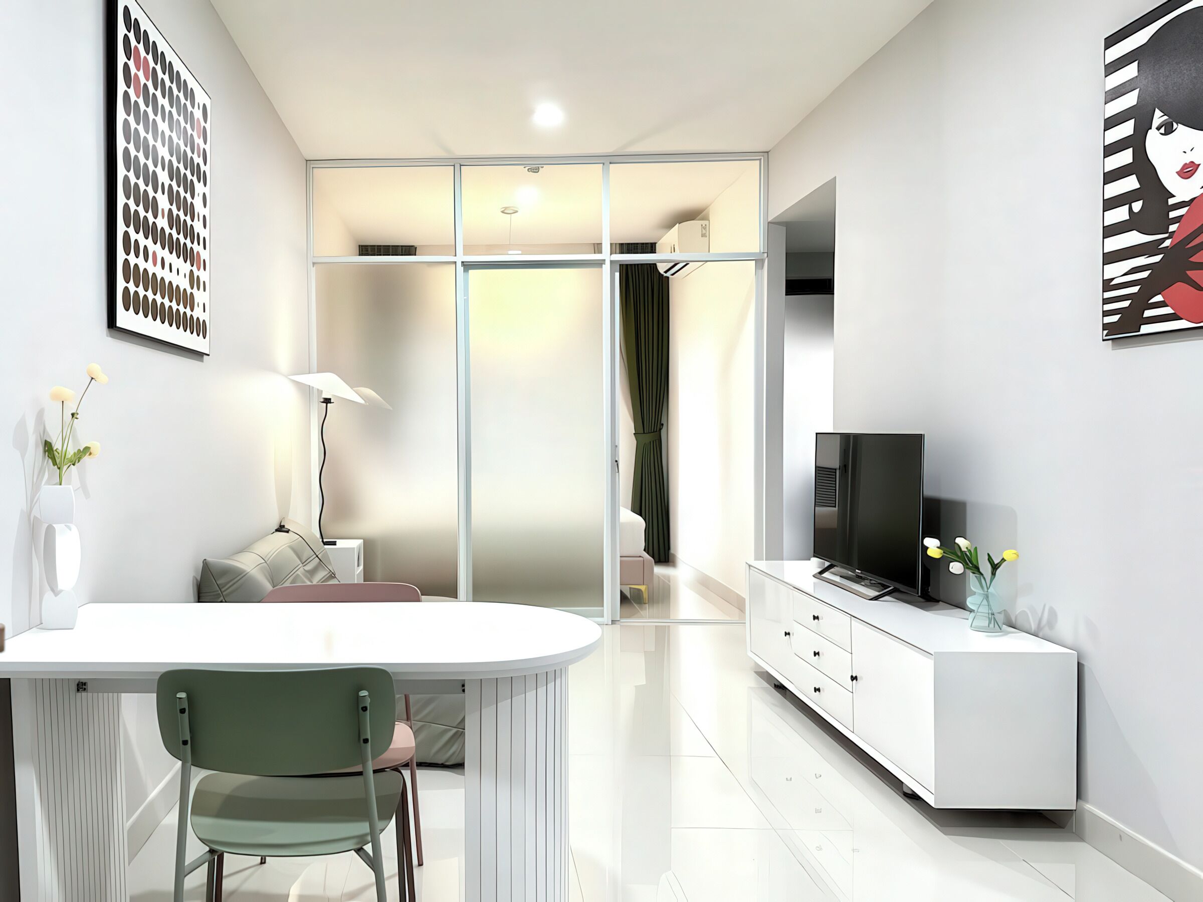 A modern, well-lit living room with a white sofa, a dining area with a table and chairs, a TV on a white cabinet, and artwork on the walls.