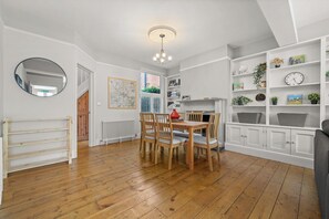 A dining area with a wooden table and chairs, a chandelier, and a white cabinet with shelves.