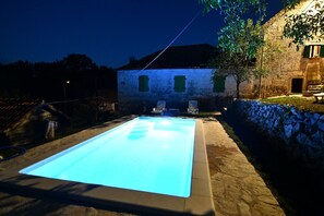 A rectangular swimming pool with a light blue tint, surrounded by stone walls and a stone pathway.