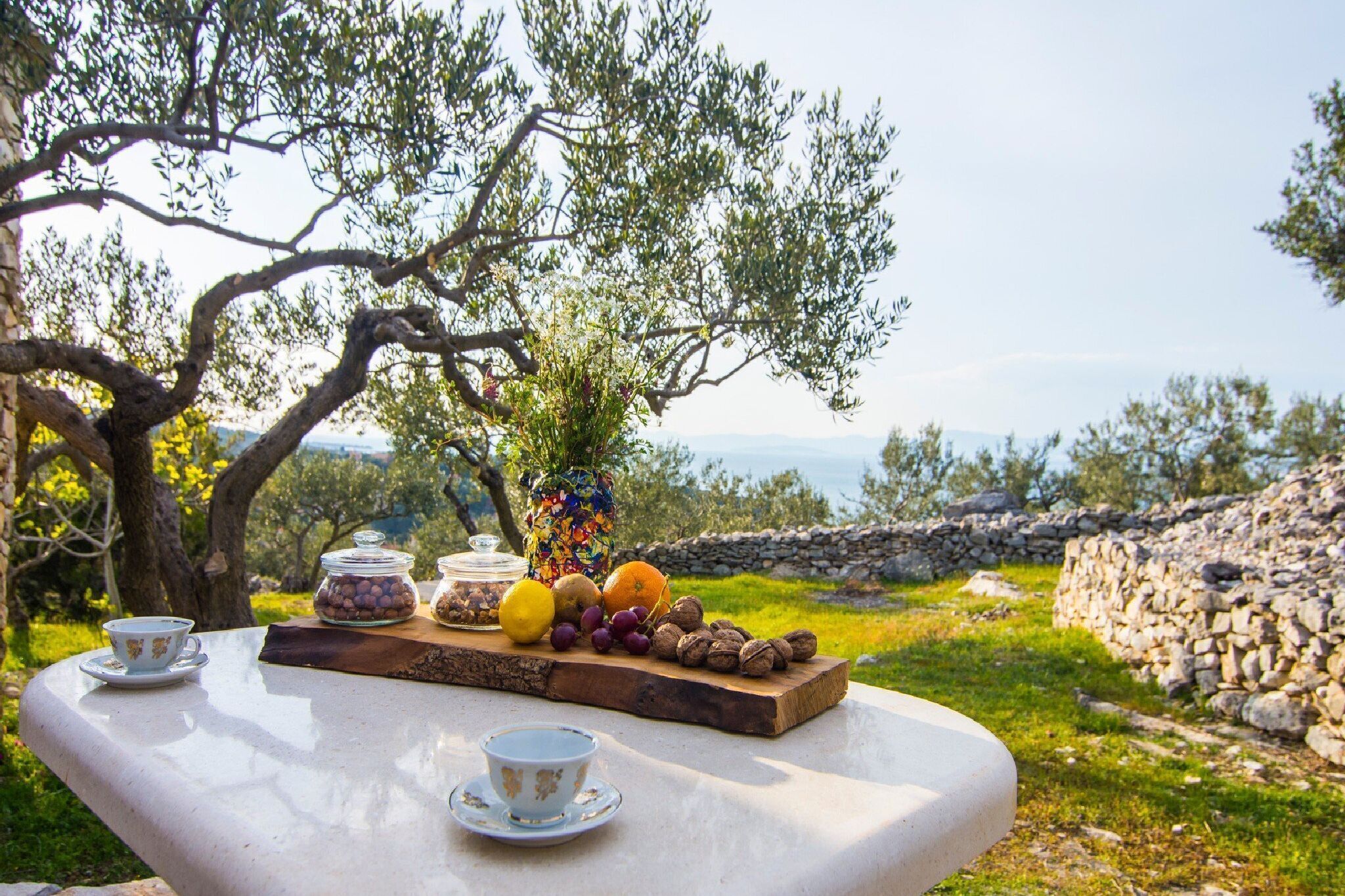 Una mesa con vista al mar, un muro de piedra y un olivo.