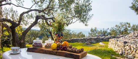 Una mesa con vista al mar, un muro de piedra y un olivo.