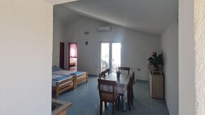 Een ruime kamer met een eettafel en stoelen, een bed met een blauwe dekbedovertrek, en een kleine kitchenette.