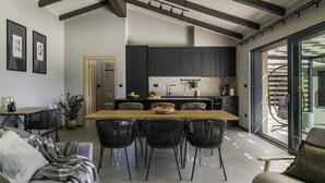 A modern kitchen with dark cabinets, a wooden dining table, and a large window. - Villa Noeli with Swimming Pool (Hum)