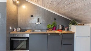 Une cuisine avec un plafond en bois, des carreaux gris, un évier, une cuisinière et un réfrigérateur.