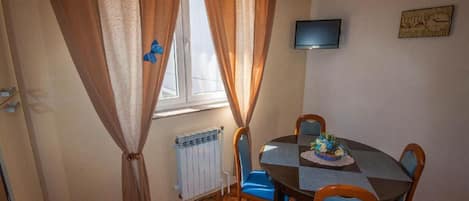 A dining area with a table, chairs, a television, and a window with curtains.