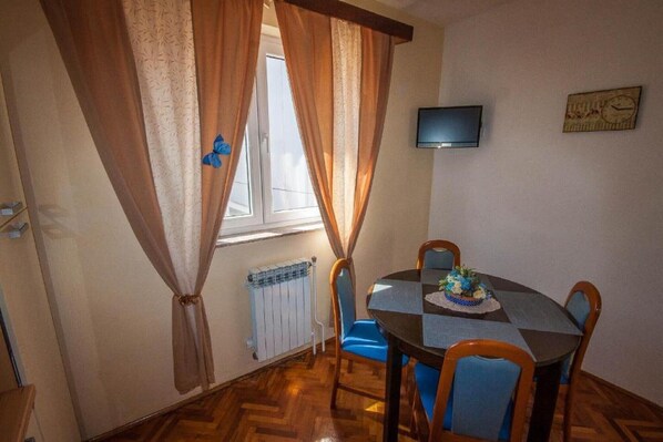 Ein Essbereich mit Tisch, Stühlen, einem Fernseher und einem Fenster mit Vorhängen.
